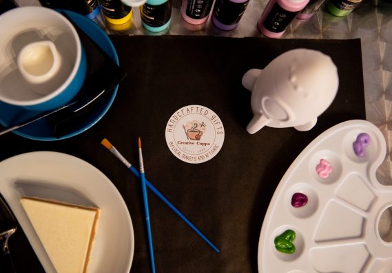 A painting activity set up for a customer with a cup of tea and a slice of cake to the side.