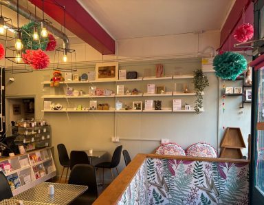 Finished: Makers wall and seating area. Finished: This wall is a sage green colour, has shelfs with maker's profiles on. Table and chairs and a counter with a cake display on top.