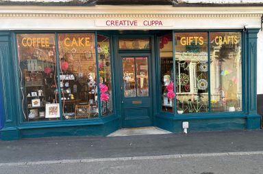 Finished: Exterior of Creative Cuppa. Finished: Exterior painted teal, Creative Cuppa in pink above the door. The words coffee, cake, gifts and crafts added to top of each window