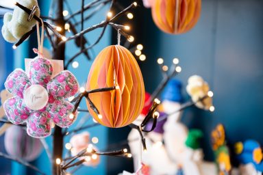 Tree with hanging decorations Artistic photo of a lit decorative twig tree with a paper decoration and handmade flower gift hanging from it. Blurred background.