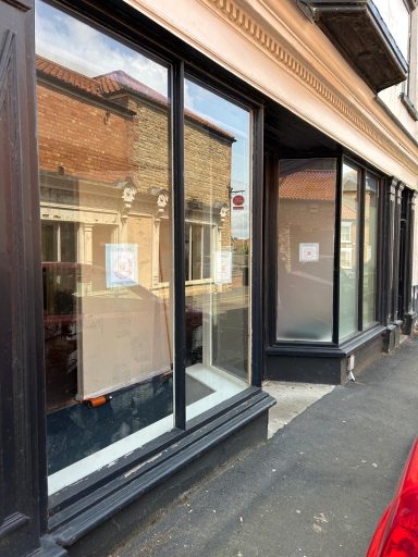 Before: Exterior shop front Before: Exterior shop front painted black with two protruding window bays and a recessed door in the middle. Small signs in each window.