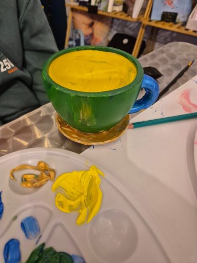 Finished customer's painted cup. Example of a customer's finished painted ceramic cup, dark green outside, yellow inside, gold plate at the bottom and a blue handle.
